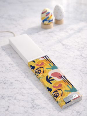 Λευκή λαμπάδα 25x4.5 με εκτύπωση Απόηχος | κίτρινη βάση με αφαιρετικά σχήματα και χρώματα | σήμα Pnevma σε ασημί.