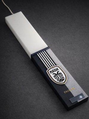 Λευκή λαμπάδα 25x4.5 με εκτύπωση ΠΑΟΚ | σκούρο φόντο με κάθετες ρίγες και κεντρικό έμβλημα | σήμα Pnevma σε ασημί.