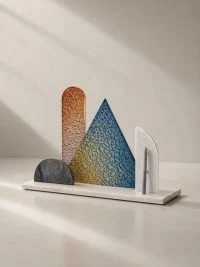 Γούρι Light Echoes Prism με καμπύλες και τριγωνικές επιφάνειες σε χάλκινους, μπλε και ουδέτερους τόνους.