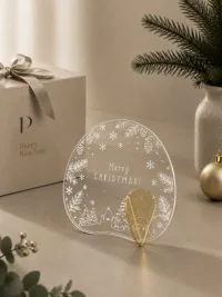 Γούρι Aurora Merry Xmas 01 με λευκές νιφάδες, μικρά έλατα και φωτεινή κυκλική εικονογράφηση.